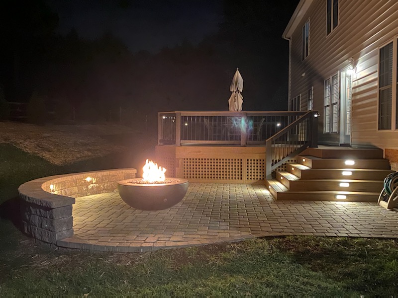 A lit-up patio with a fire bowl and a deck, showing the work of a deck and patio builder in Charlotte, NC.